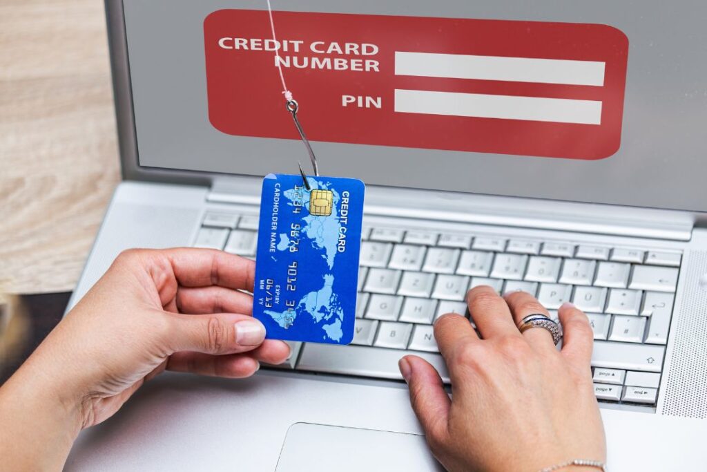 a person typing in their credit card information into a fake website as part of a phishing scam with a fish hook attached to their credit card as symbolism of phishing