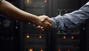 Two people shake hands in front of a wall of servers, having just provided IT services.
